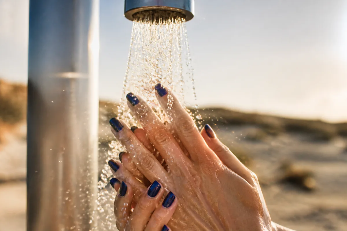 Rinçage des mains à l’eau douce sous une douche de plage en fin de journée