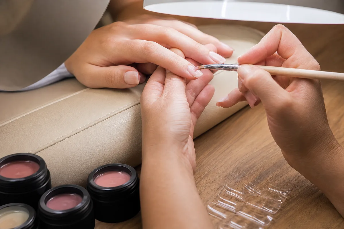 Détail d&rsquo;une pose d&rsquo;ongles en gel sous lampe LED sur un poste de manucure
